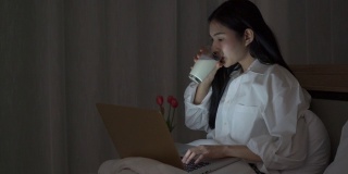快乐的女人，晚上在笔记本电脑上工作，喝着牛奶