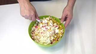 一个男人在做沙拉。将剁碎的蟹棒，玉米，北京卷心菜和蛋黄酱混合在一个容器里。视频素材模板下载