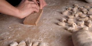 用全麦面粉制作自制素食意面的过程。家庭厨师在木砧板上擀面团，传统的意大利面食，女人在厨房做饭