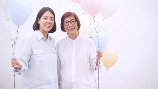 亚洲活跃的老年妇女与她的中年女儿与彩色气球。快乐的老年人生活方式