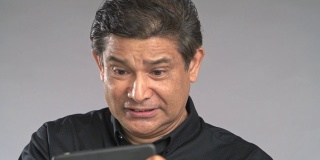 近景老人在手机上玩手机游戏，输了游戏，失望孤立在灰色背景中。穿着黑衬衫的亚洲人。