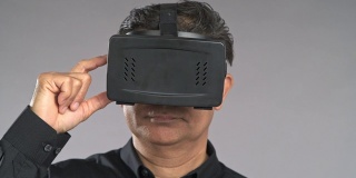 近景老人使用虚拟现实耳机，按下按钮，环顾四周，孤立在灰色背景中。穿着黑衬衫的亚洲人。
