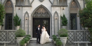 亚洲新娘和新郎携手走出教堂。相爱的新婚夫妇。手持拍摄，真实生活