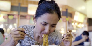 年轻的亚洲女人饿着吃炒面猪肉和甘蓝浸在肉汁(Radna)著名的泰国食物，吃看起来很好吃。