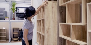 亚洲女性顾客购买和选择桌子和书架木材家居装饰。亚洲女性在商店购买五金和家具。