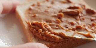 把花生酱涂在烤面包上，做三明治