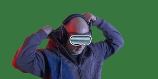 秃头男人听音乐在耳机和VR眼镜在绿色的chromakey背景。戴着黑色兜帽和虚拟现实眼镜的人在耳机里听音乐。Alpha通道，绿色屏幕。