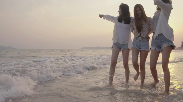 微笑快乐的亚洲朋友群年轻的女人一起走在海边的海滩上夏天度假日落剪影黄昏假日旅游享受生活周末活动人们的生活方式，慢镜头4K