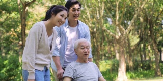 年轻的亚洲夫妇帮助轮椅上的父亲站起来