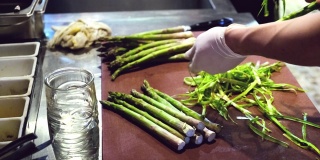 在厨房的背景上，手正在用一把特制的刀削绿芦笋
