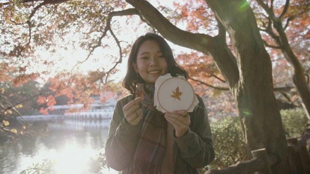 在一个阳光明媚的日子在东京城市的公园里，微笑的年轻亚洲妇女拿着绣框的枫叶图案肖像。