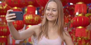 一名年轻女子站在许多东亚人用来庆祝农历新年的红色中国灯笼中间自拍。亚洲之旅概念