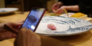 在一家日本小餐馆里，一位女士正在用智能手机拍寿司