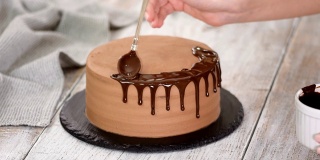在巧克力蛋糕上涂上融化的巧克力。往蛋糕上倒巧克力的女人。自制可可分层蛋糕。