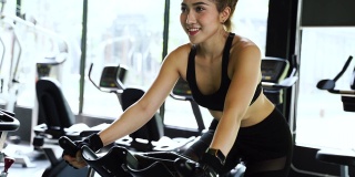 迷人的亚洲女人在健身房骑动感单车