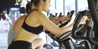 迷人的亚洲女人在健身房骑动感单车，看着镜头。健康和减肥的生活方式