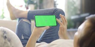 女人在沙发上用绿色屏幕的智能手机