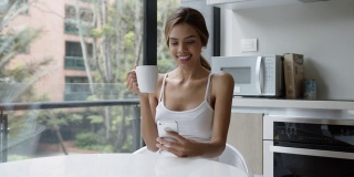 美丽的拉丁美洲女人放松在家查看她的社交媒体，同时喝咖啡