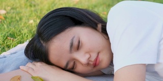 缓慢的动作年轻的亚洲女人睡觉，而躺在地面公园在春天，夏天，特写亚洲女孩午睡和躺在花园户外休息的背景，女性青少年休息，放松，幸福健康的生活方式