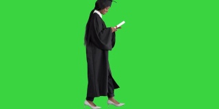 年轻的美国黑人女学生穿着黑色毕业礼服，拿着文凭，在绿色屏幕上使用手机，Chroma Key