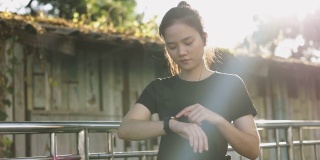 迷人的年轻亚洲女运动员在智能手表上查看心率。日落时分在街上慢跑锻炼的生活方式。