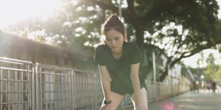 亚洲女运动员在城市的夕阳下进行有氧运动后精疲力竭地跑步休息。