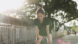 亚洲女运动员在城市的夕阳下进行有氧运动后精疲力竭地跑步休息。视频素材模板下载