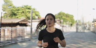 快乐女孩运动员戴着耳机，用智能手机听着音乐在城市外面跑步。慢跑的生活方式健康。