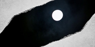 这段创造性的视频拍摄了夜空中一轮明亮的满月和漂浮的云，通过一个边缘撕裂的洞可以看到，这个洞是用复古的旧纸张做的。