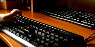 木桌上的黑色键盘特写，一个小孩子的手敲击键盘，在游戏的帮助下，孩子们早期掌握和学习电脑。