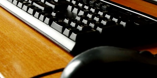 木桌上的黑色键盘特写，一个小孩子的手敲击键盘，在游戏的帮助下，孩子们早期掌握和学习电脑。