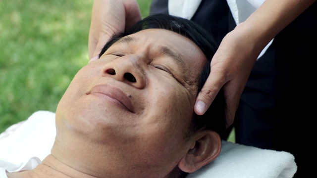 老人在户外做头部按摩。亚洲男人躺在床上。享受自己的时间。高级生活方式。