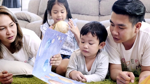 全家一起在客厅看书。亚洲男人和女人和他们的儿子和女儿躺在地板上看书。把页面。