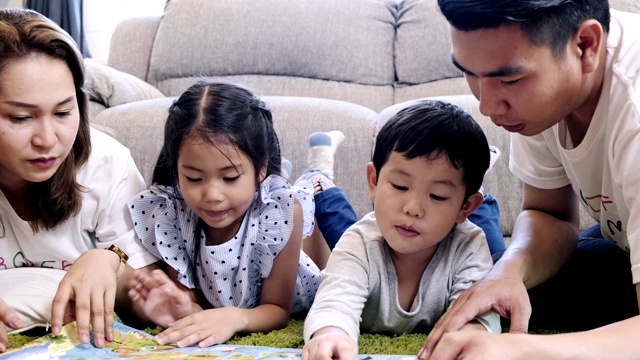 全家一起在客厅看书。亚洲男人和女人和他们的儿子和女儿躺在地板上看书。一个孩子正在看地图。