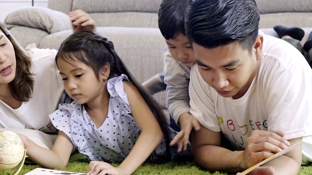 全家一起在客厅看书。亚洲男人和女人和他们的儿子和女儿躺在地板上看书。快乐的心情。