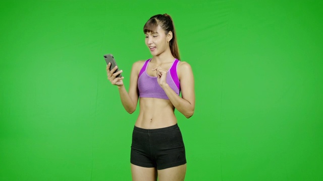 Fit woman浏览手机，惊喜，销售，绿屏背景，Fit body, social media communication。亚洲女运动员穿着紫色的衣服站在镜头前。