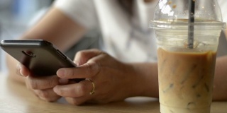一名亚洲女性一边喝冷饮一边用智能手机发短信进行交流和在线社交聊天。