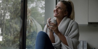 美丽的女人在家里盖着被子，享受着茶，看着窗外的景色，做着白日梦