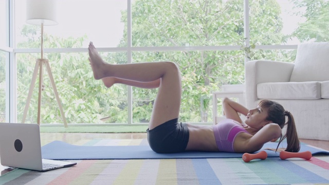健身女性锻炼，空气自行车踢腿，腹肌，锻炼，坐起来和下来，听从笔记本电脑的指示。美丽的亚洲女人在体育。