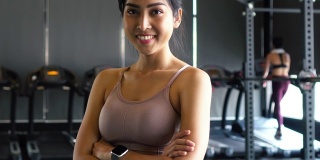 微笑和坚定的年轻亚洲女运动员看着镜头，双臂交叉，站在健身房健身中心