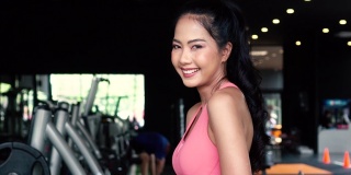 微笑和坚定的年轻亚洲女运动员看着镜头，双臂交叉，站在健身房健身中心