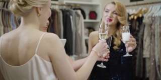三个乐观的白人女性在时尚精品店用香槟碰杯。快乐富有的女性朋友在购物中心庆祝购物。财富,生活方式,消费主义。Slowmo。
