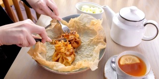 Woman is eating julienne baked in dough served on a plate on baker paper with tea and butter. Hands close-up.