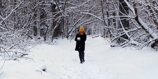 一个快乐的女孩走过冬天的森林，微笑着，有一个好心情，玩雪，吹雪花在雪花的背景