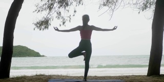 亚洲女人看海练习瑜伽在海滩上冥想灵活平衡，树姿势/ Vrksasana，健康积极的生活方式概念