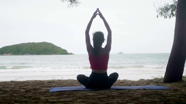 亚洲女人看海练练瑜伽，在沙滩上冥想柔韧平衡，瑜伽坐半莲花运动，健康积极的生活方式理念