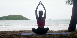 亚洲女人看海练练瑜伽，在沙滩上冥想柔韧平衡，瑜伽坐半莲花运动，健康积极的生活方式理念