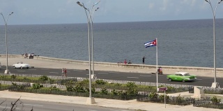 老爷车行驶在哈瓦那主要公路上，经过古巴国旗