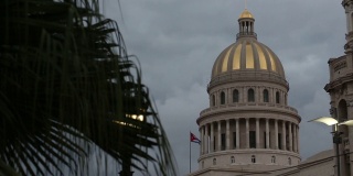 跟踪经过热带树显示古巴国会大厦的穹顶和国旗在不祥的云