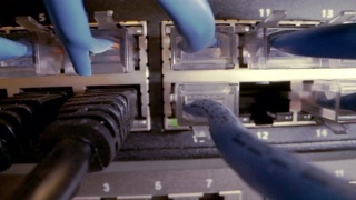 在IT组网柜背景中，Cat5e以太网线缆插入交错的、杂乱的高速千兆因特网Cat5数据补丁线缆闪烁的网络交换机视频素材模板下载